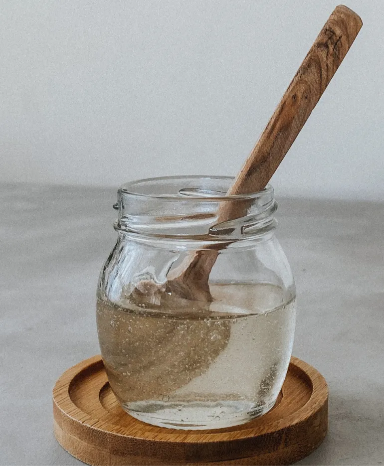 Glass jar of golden honey with a wooden spoon