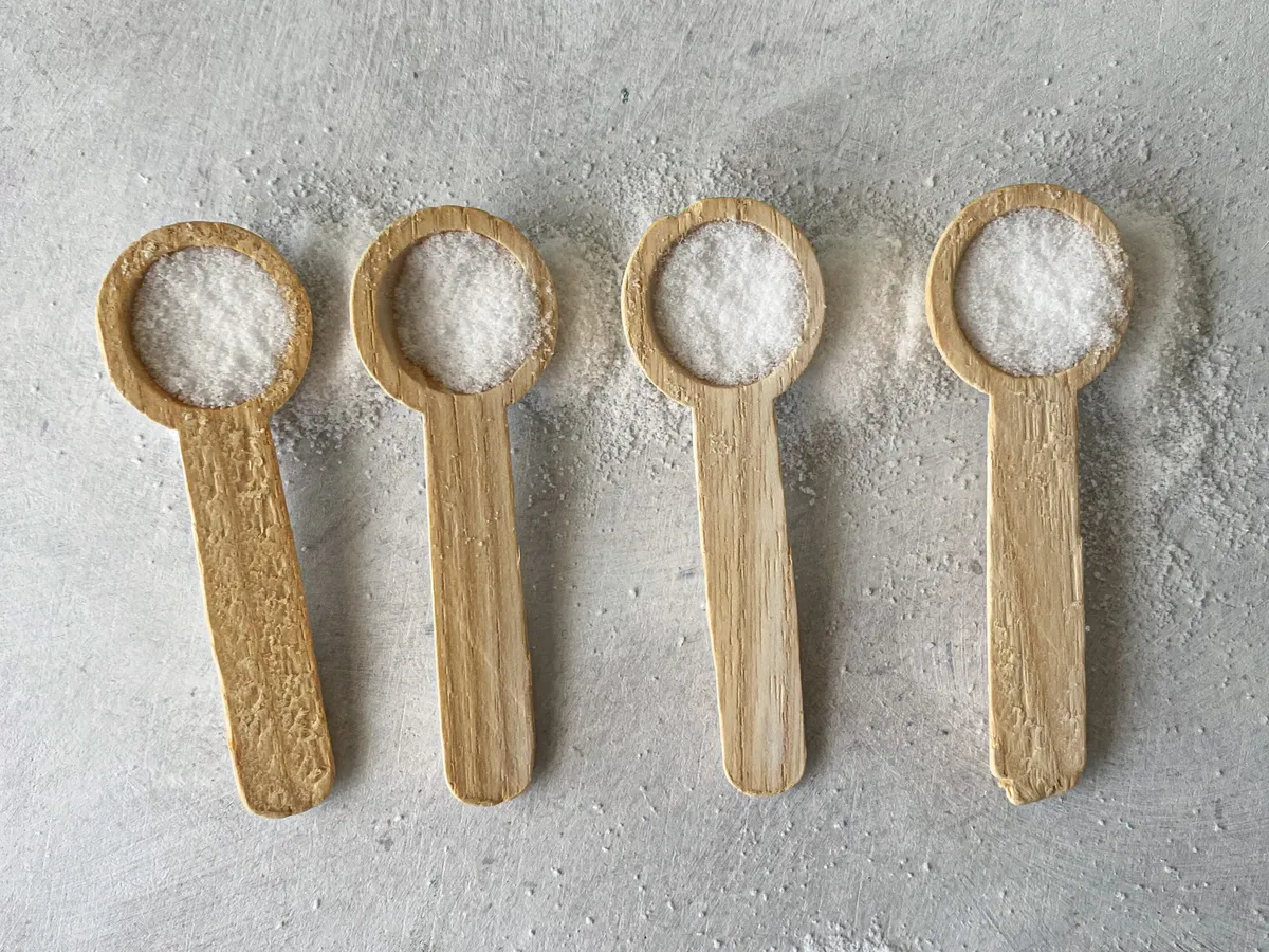 Four wooden spoons of white sweetener crystals on a grey surface
