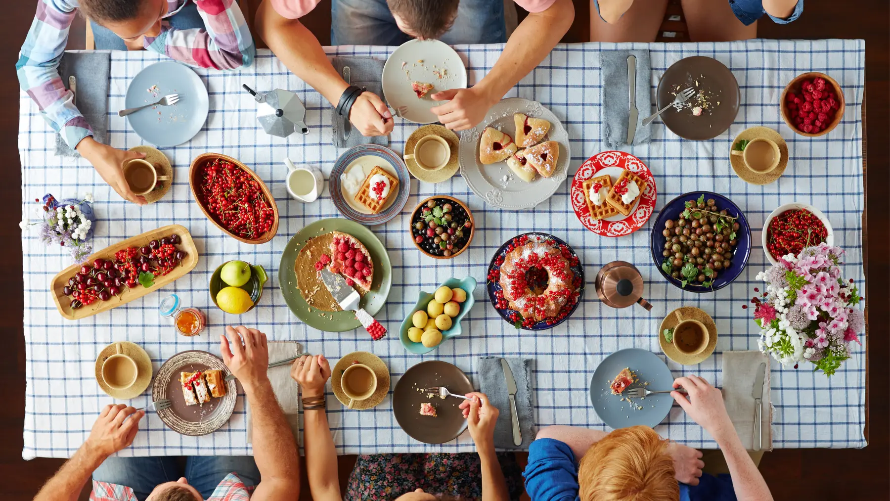 Friends sharing a breakfast table of pastries, berries, fruit and coffee, seen from above