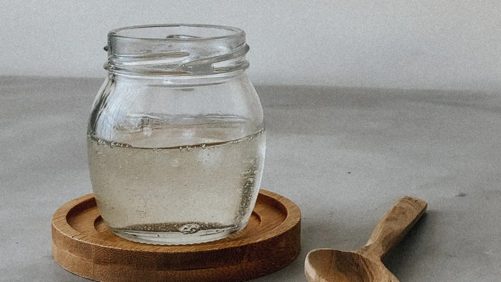A glass jar of clear, honey-like liquid on a wooden coaster with a wooden spoon