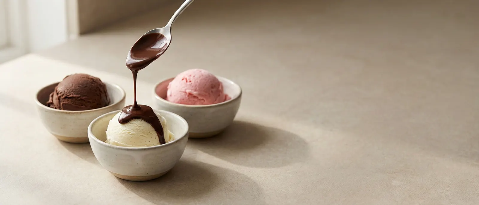 Chocolate sauce drizzled from a spoon over bowls of ice cream