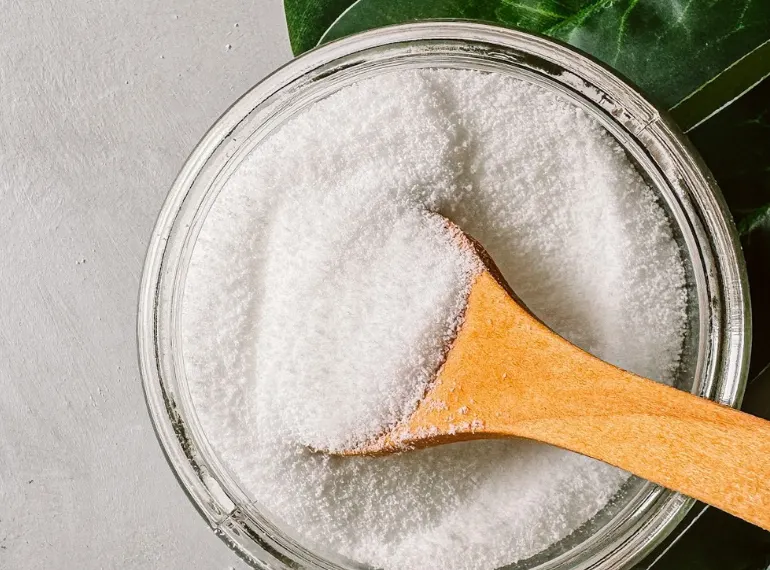 Top view of a wooden spoon scooping white sweetener from a glass bowl