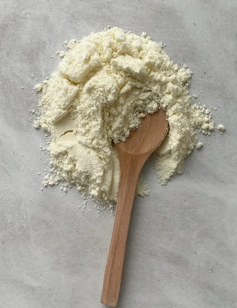 A heap of cream-coloured protein powder with a wooden spoon