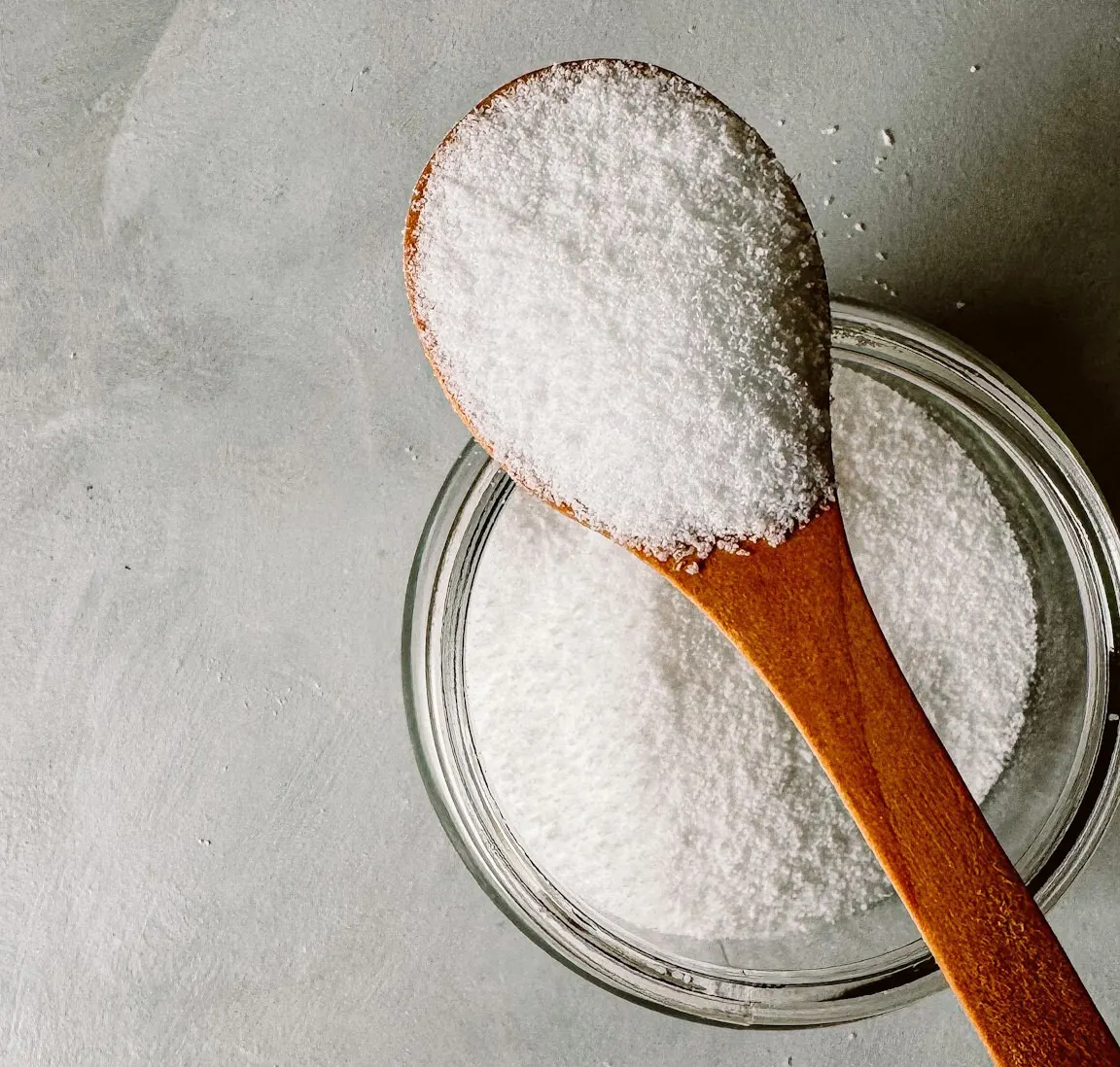 White crystalline powder on a wooden spoon over a glass bowl