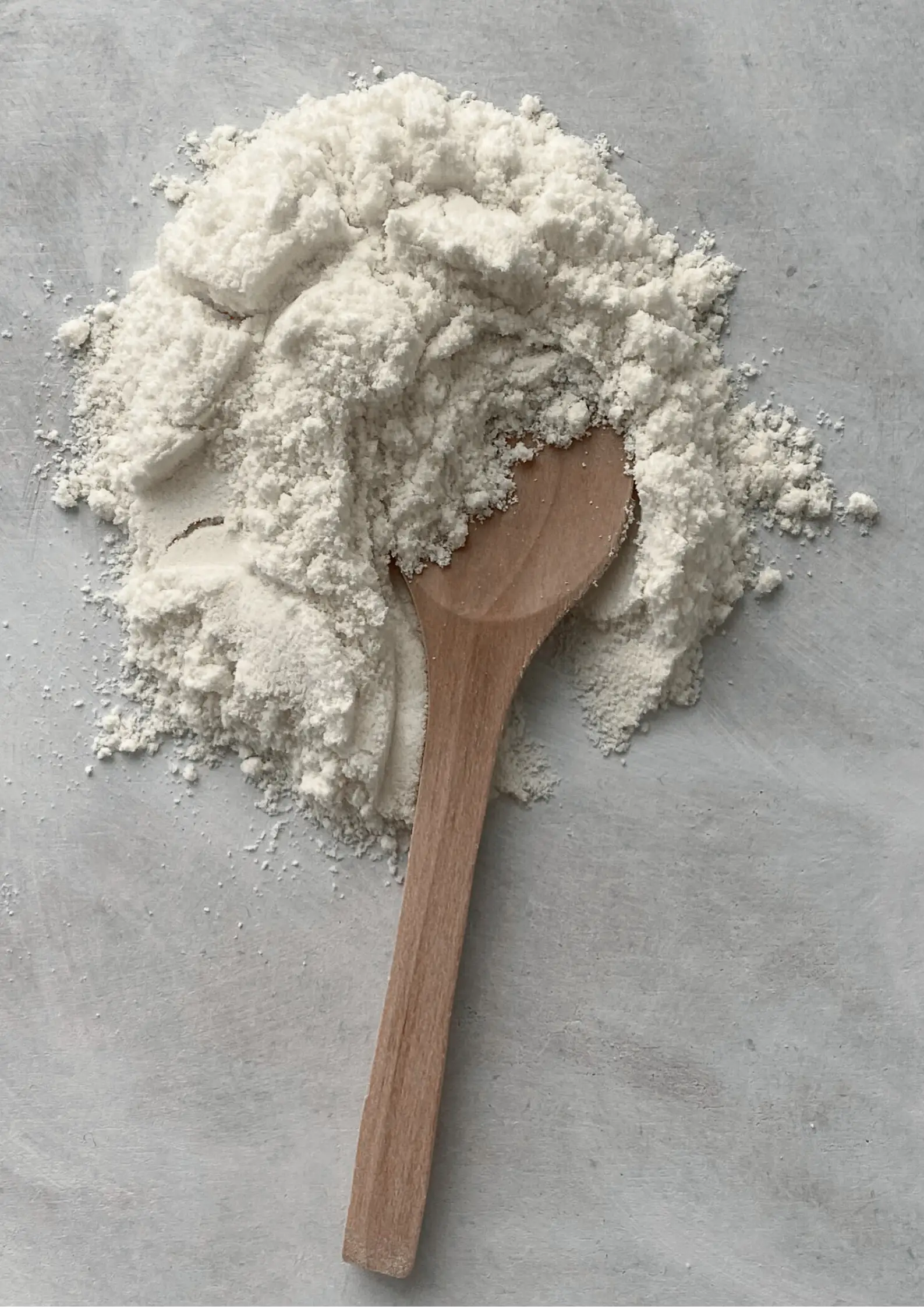 A pile of white powder with a wooden spoon partly buried in it, on a light grey surface