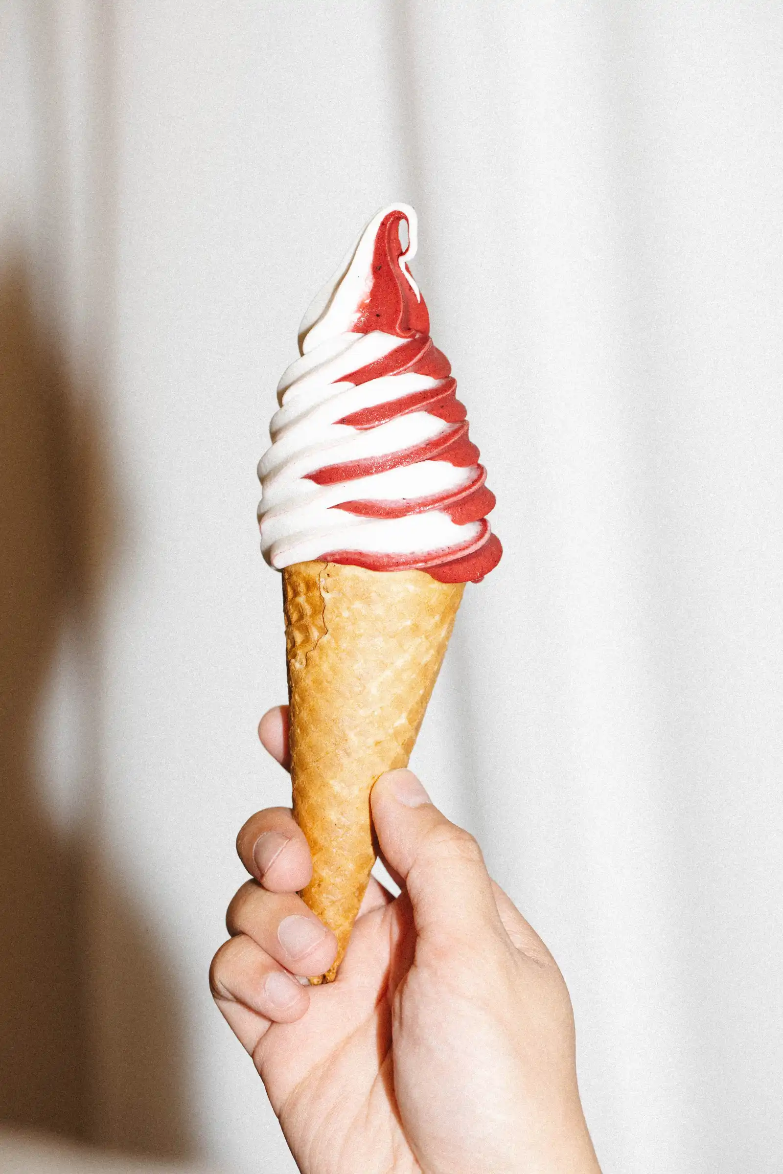 A hand holding a soft-serve ice cream cone with a red swirl
