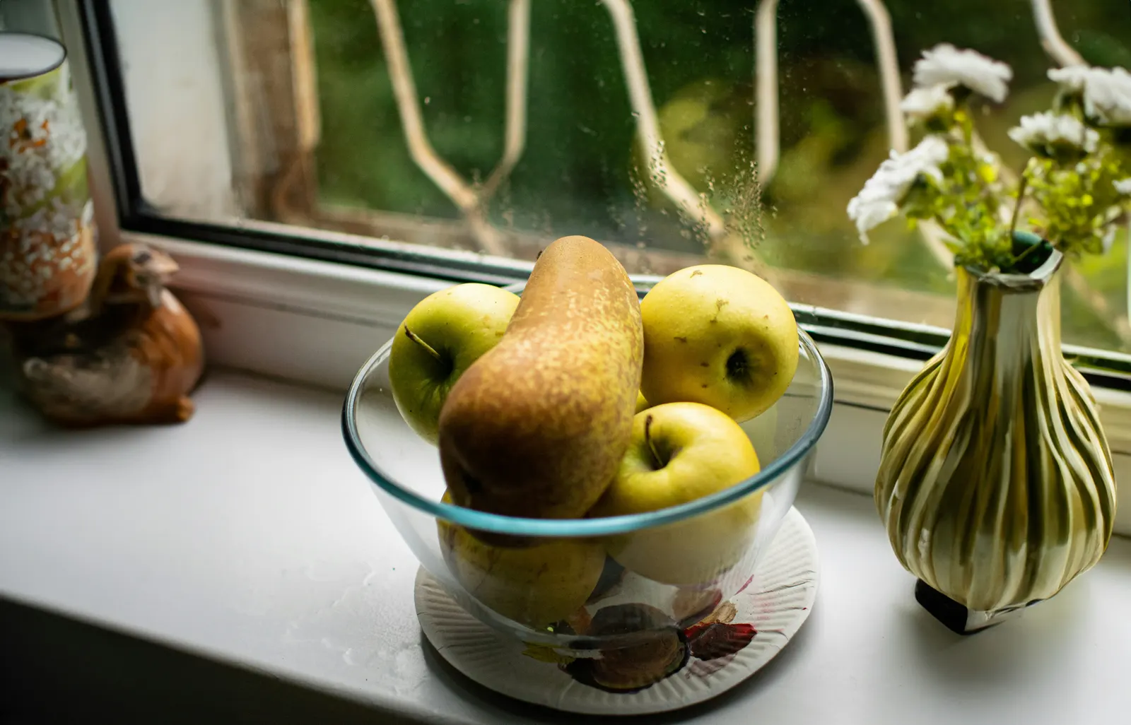 A glass bowl of apples and pears on a sunny windowsill